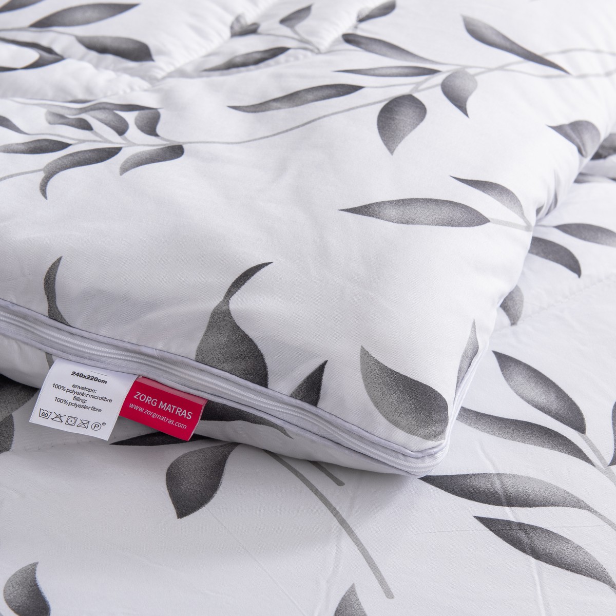 Detailfoto van het vierseizoenen dekbed Nora met zichtbaar kwaliteitslabel en rits aan de onderzijde van de bladmotief overtrek.