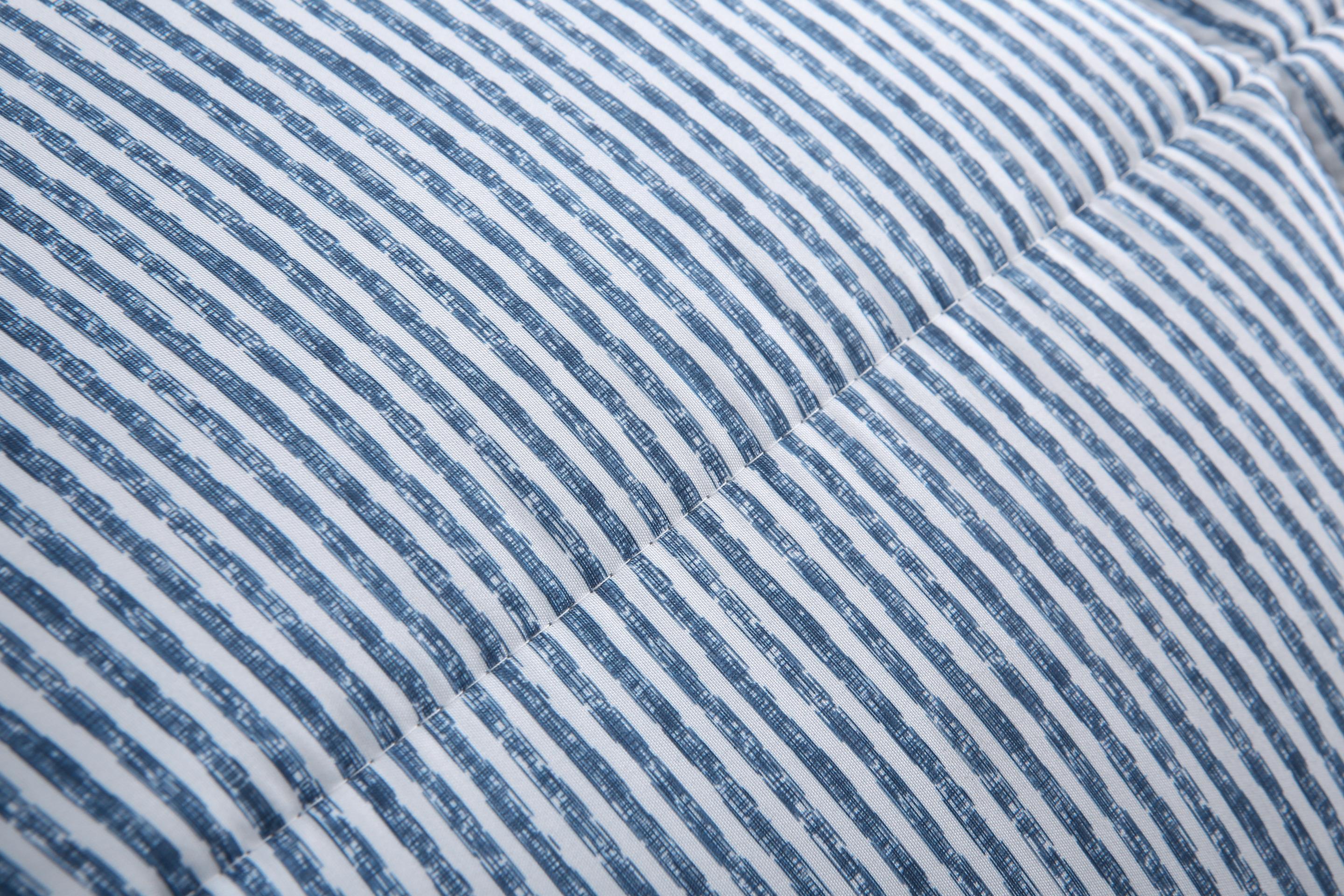 Detailweergave van het blauw gestreepte dekbed met vaste hoes en twee grijze hoofdkussens op de achtergrond.